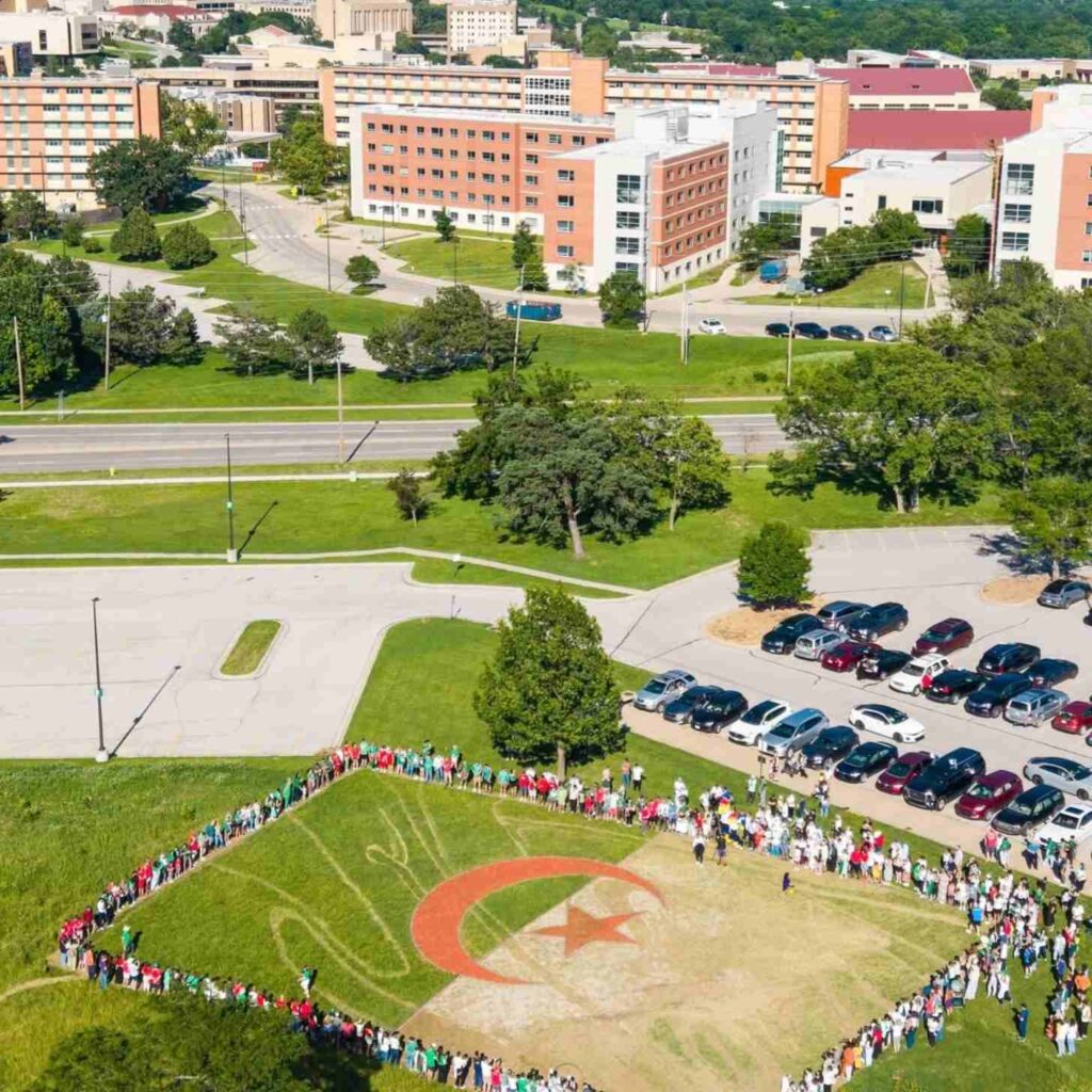 Vista aérea de um campus universitário com uma multidão formando um contorno humano em um campo pintado com a bandeira da…